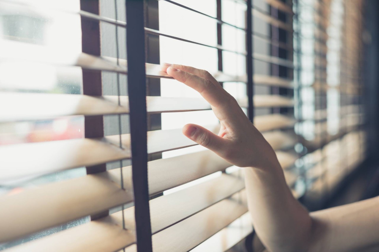 Someone's hand resting lightly on a set of wooden window blinds at In The Shade near Stuart Florida (FL)